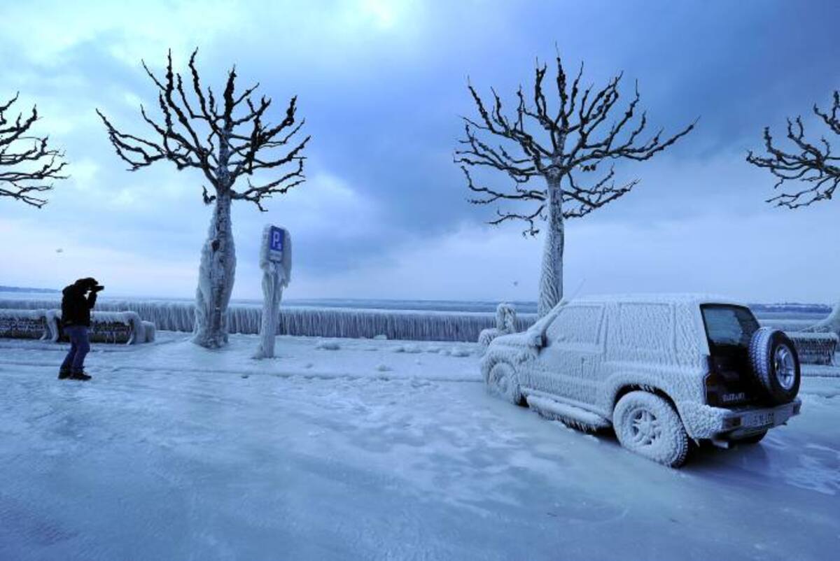 A man snaps a picture of an ice covered car on the frozen waterside promenade at Lake Geneva in the city Versoix on early February 5, 2012. The death toll from the vicious cold snap across Europe has risen to more than 260, with the winter misery set to hit thousands of those seeking to escape it as air traffic was hit. AFP PHOTO / FABRICE COFFRINI