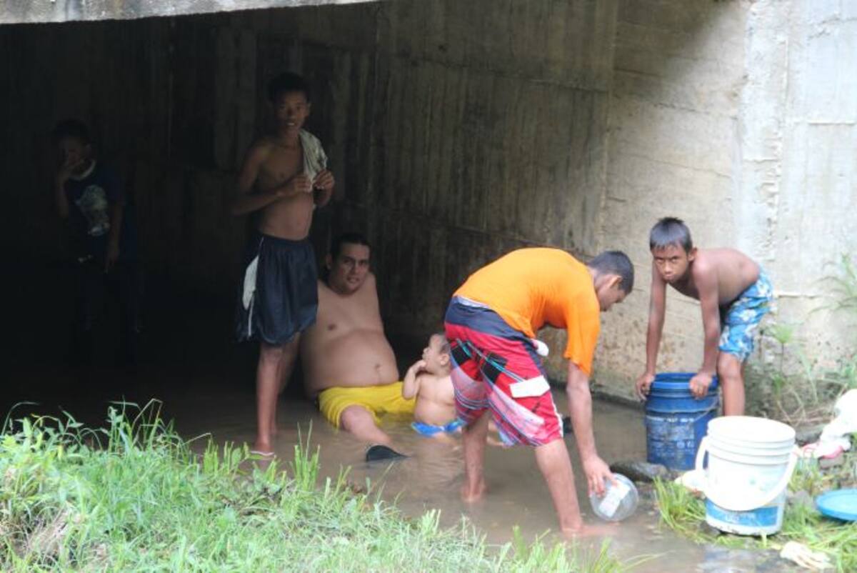 Un grupo de personas toma un baño en un caño debajo de un puente. Gabriel J. García G.