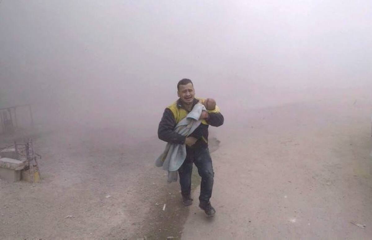 Un paramédico transporta a su hijo herido, huyendo de la escena después de que un ataque aéreo golpeó un suburbio cercano a Damasco. AP Uncredited