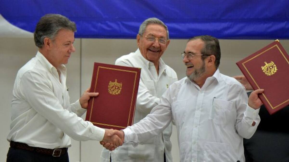 Juan Manuel Santos y Timochenko estrechan las manos frente al presidente de Cuba, Raúl Castro. Archivo.