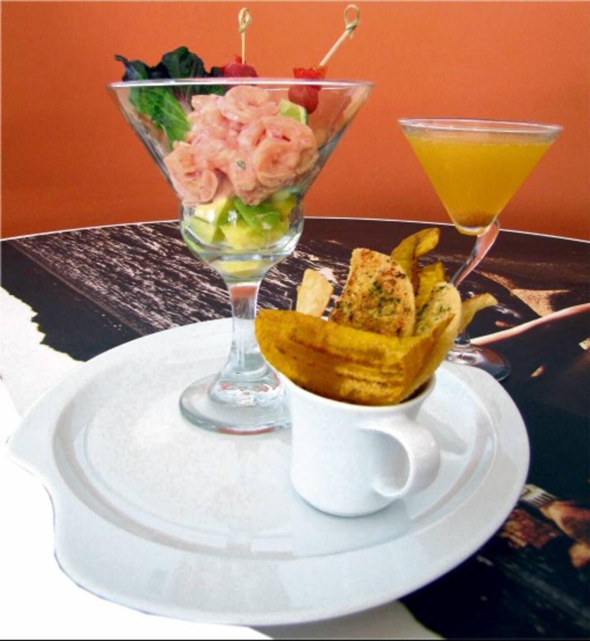 Coctel de camarón con mousse de aguacate, acompañado de chips de plátano y casabe gratinado. La bebida es un martini de uchuvas.