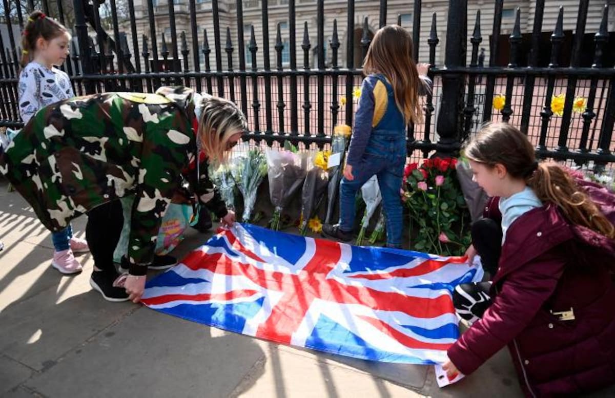 La gente pone una bandera junto a flores y mensajes de condolencia frente al Palacio de Buckingham tras el fallecimiento del Príncipe Felipe de Gran Bretaña, en Londres, Gran Bretaña. EFE / EPA / NEIL HALL