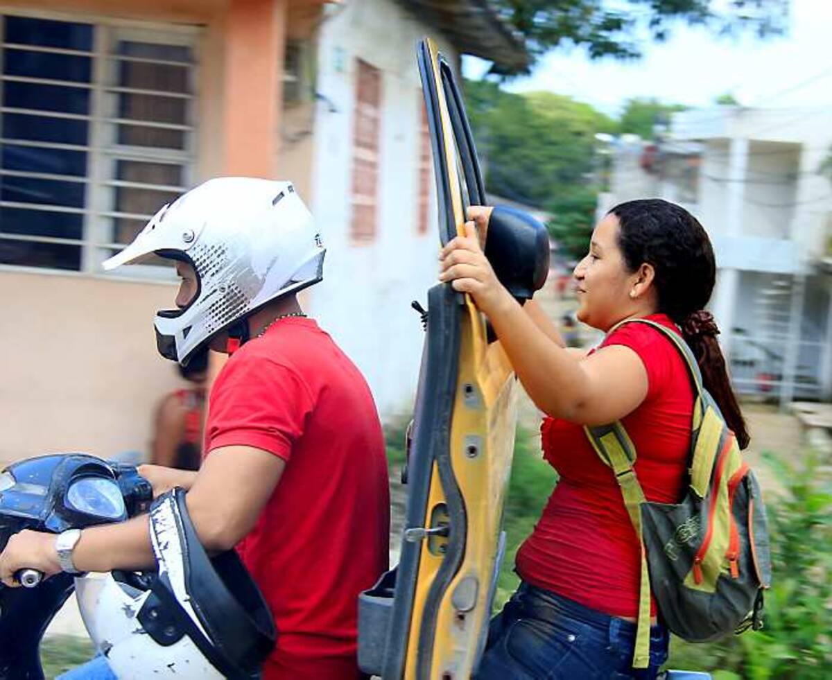 La parrillera de esta moto carga la puerta de un taxi ‘zapatico’ y pone en riesgo su vida, dado que no va agarrada al vehículo y tampoco lleva casco que la proteja en caso de accidente. LUIS EDUARDO APARICIO - EL UNIVERSAL