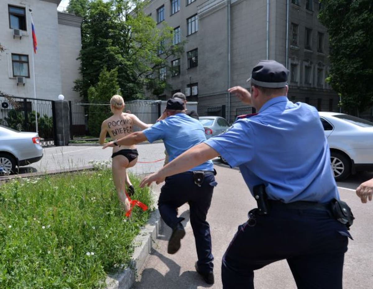 Un miembro de la organización feminista Femen con las palabras "¡Adelante Rusia!" escrito en su espalda, se escapa de la policía quienes tratan de detenerla después de que ella gritara "Vladimir te amo!" realizando con una cinta la interpretación de la gimnasta rusa Alina Kabayeva. AFP SERGEI SUPINSKY