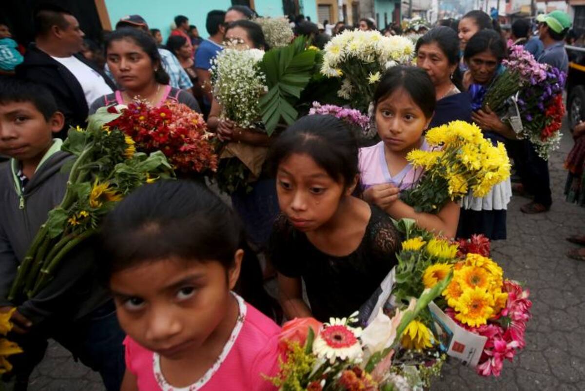 Un grupo de niños carga arreglos florales mientras caminan junto a cientos de personas que acompañan los féretros de siete de las víctimas de la erupción del Volcán de Fuego. EFE Esteban Biba