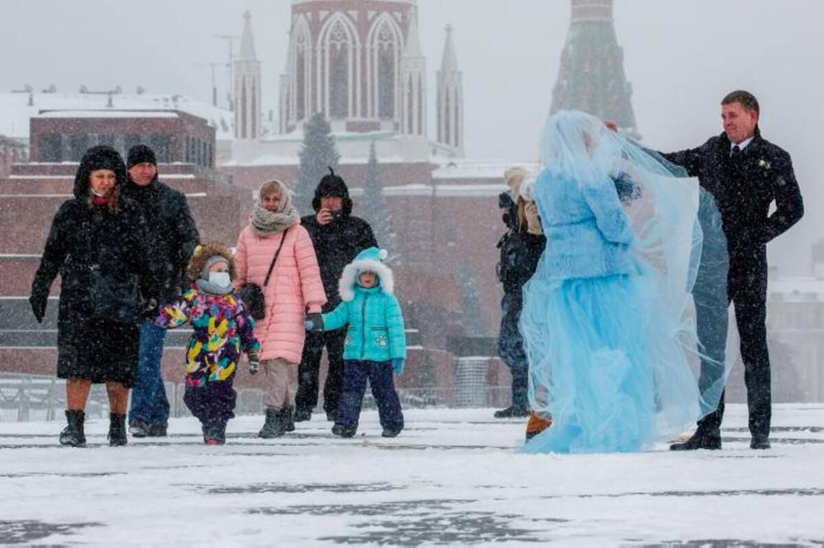Recién casados posan para fotografías en la Plaza Roja durante una fuerte nevada en Moscú. EFE SERGEI ILNITSKY