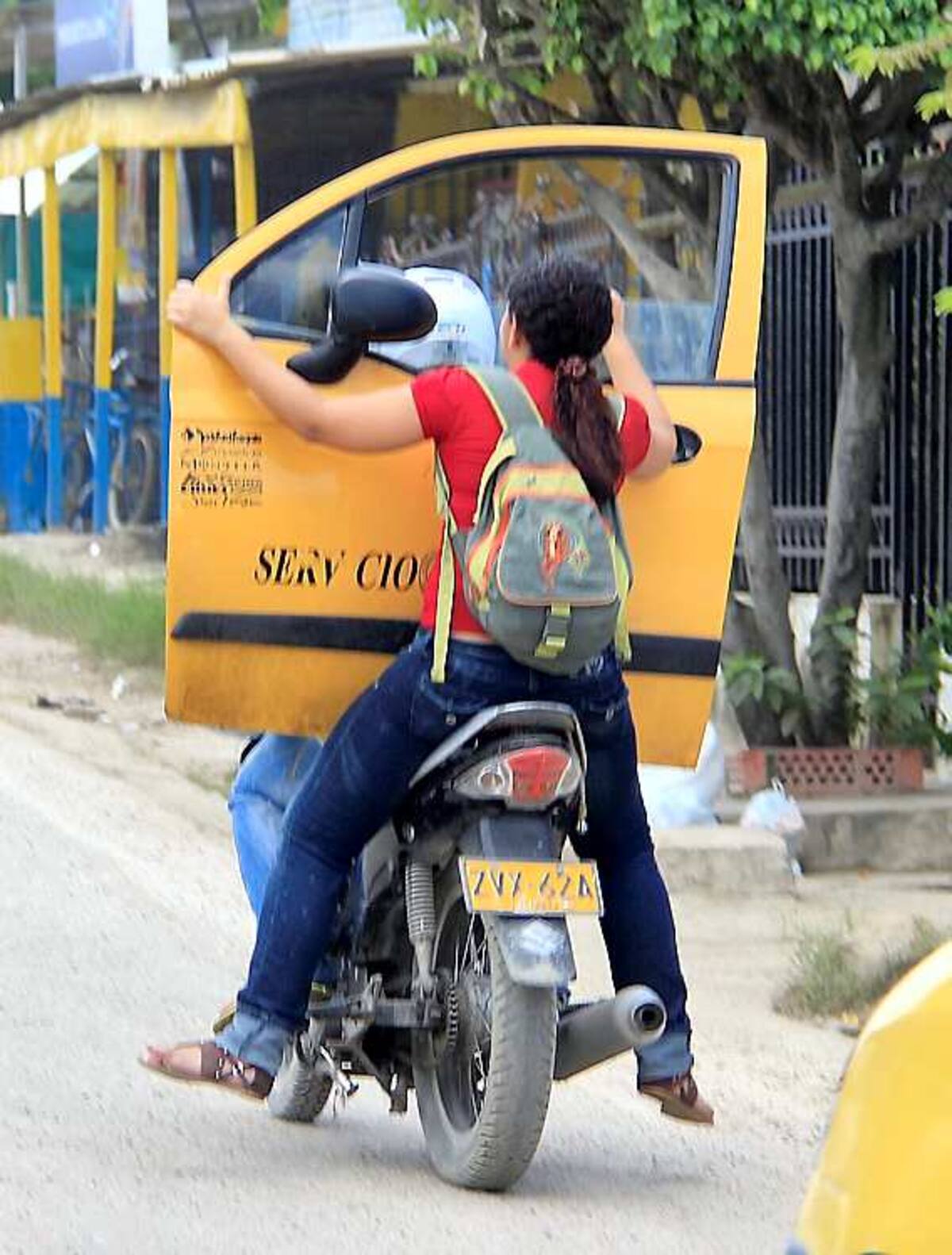 La parrillera de esta moto carga la puerta de un taxi ‘zapatico’ y pone en riesgo su vida, dado que no va agarrada al vehículo y tampoco lleva casco que la proteja en caso de accidente. LUIS EDUARDO APARICIO - EL UNIVERSAL