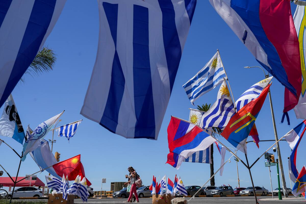 Los peatones pasan junto a la bandera nacional de Uruguay y carteles de partidos políticos en Montevideo. //AP