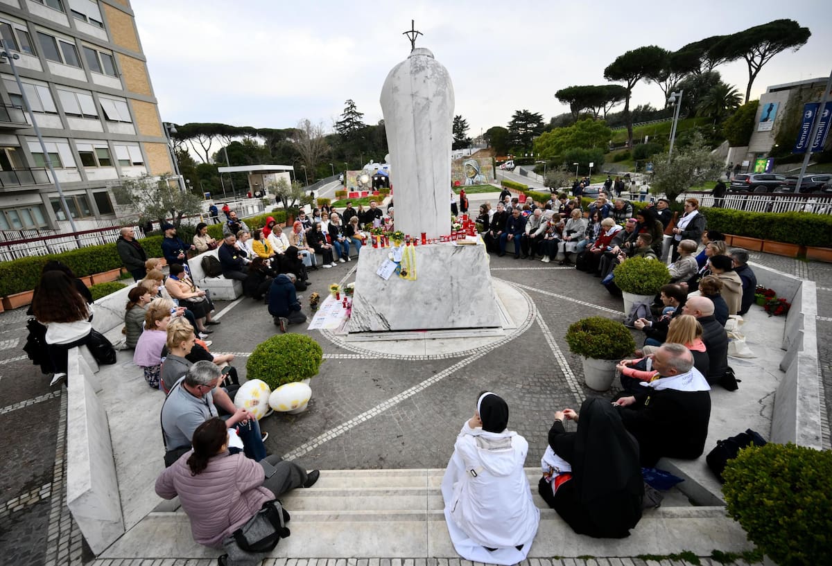 Un grupo de peregrinos se reúne junto a la estatua de Juan Pablo II en la entrada del Hospital Gemelli, donde está hospitalizado el papa Francisco. //EFE