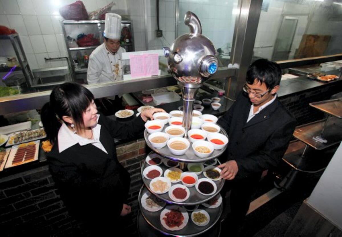 Mientras los clientes ingresan al restaurante iluminado a medias con luces de neón en un ambiente futurista, una robot con largas pestañas recibe a la gente y dice con voz electrónica “bienvenido".