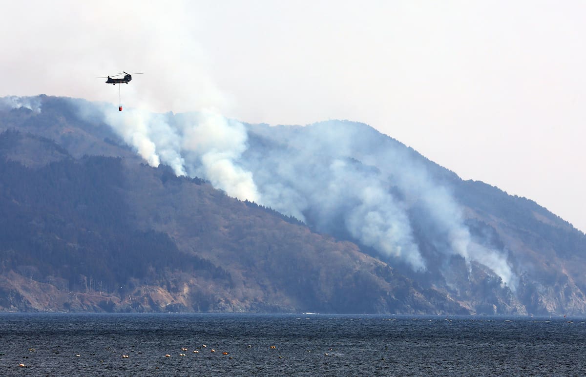 Un helicóptero militar asiste en los esfuerzos de extinción de incendios mientras el humo se eleva desde las colinas en Ofunato, prefectura de Iwate, noreste de Japón. //EFE
