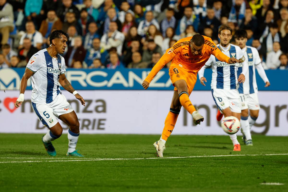 El delantero francés del Real Madrid, Kylian Mbappé (c), remata ante los jugadores del Leganés durante el encuentro correspondiente a la jornada 14 de Laliga EA Sports. // EFE / J.J. Guillen.