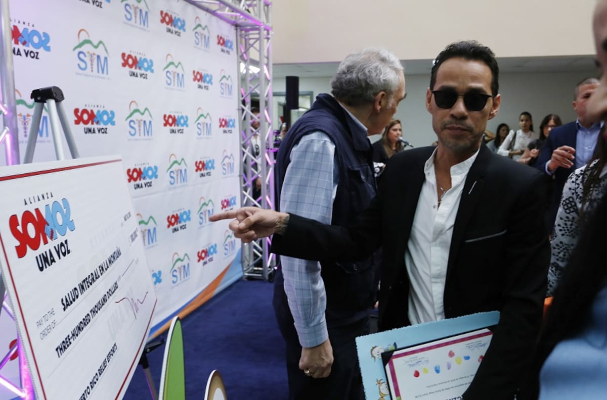 El cantante estadounidense de origen puertorriqueño Marc Anthony señala al cheque de 300 mil dólares que donó junto a la clínica móvil hoy, jueves 10 de mayo de 2018, en Orocovis (Puerto Rico). EFE