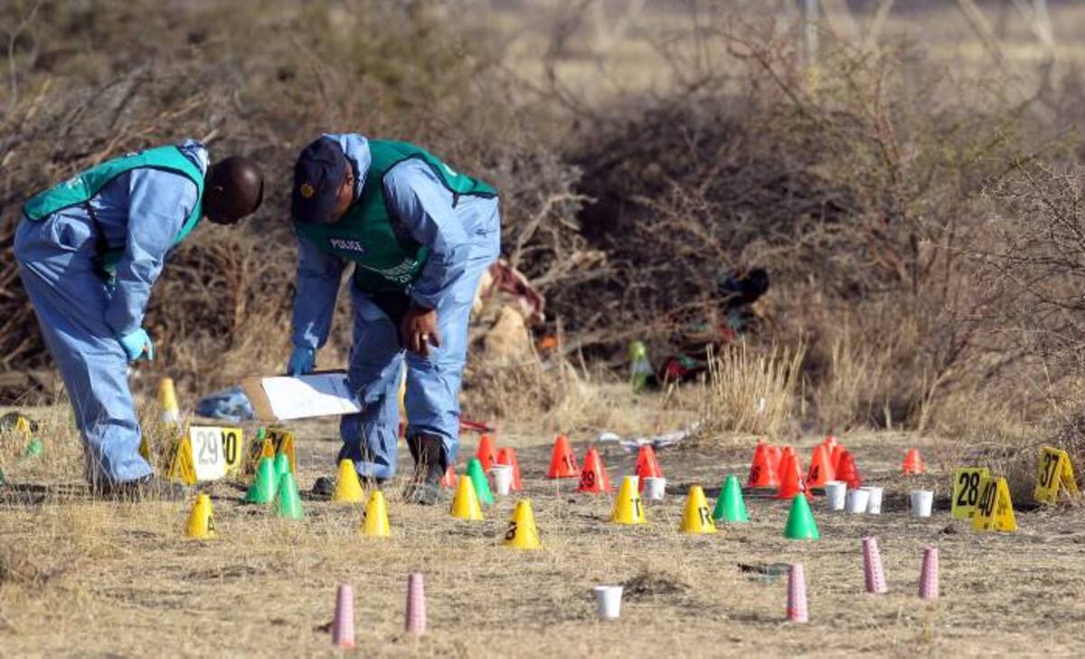 Forenses sudafricanos analizan la zona de la tragedia, donde 36 personas murieron el jueves después que la policía sudafricana abrió fuego contra trabajadores en huelga en la mina de platino Marikana. AP Themba Hadebe