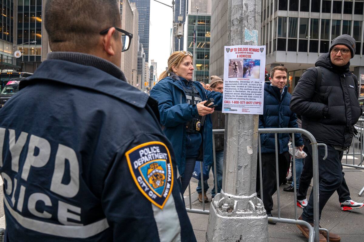 Una agente del Departamento de Policía de Nueva York (NYPD) cuelga un cartel de recompensa para quien ayude en la captura de Luigi Mangione. //EFE