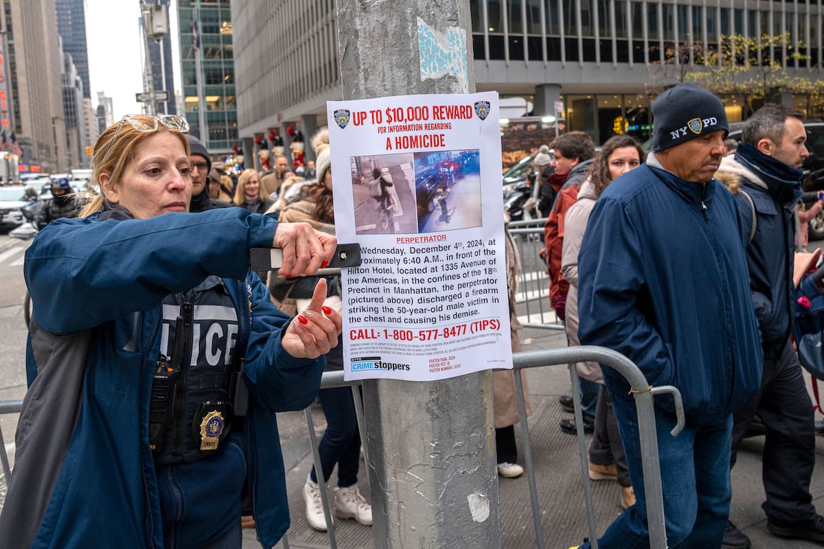 Una agente del Departamento de Policía de Nueva York (NYPD) cuelga un cartel de recompensa para quien ayude en la captura del asesino del director ejecutivo de la aseguradora UnitedHealthcare. //EFE