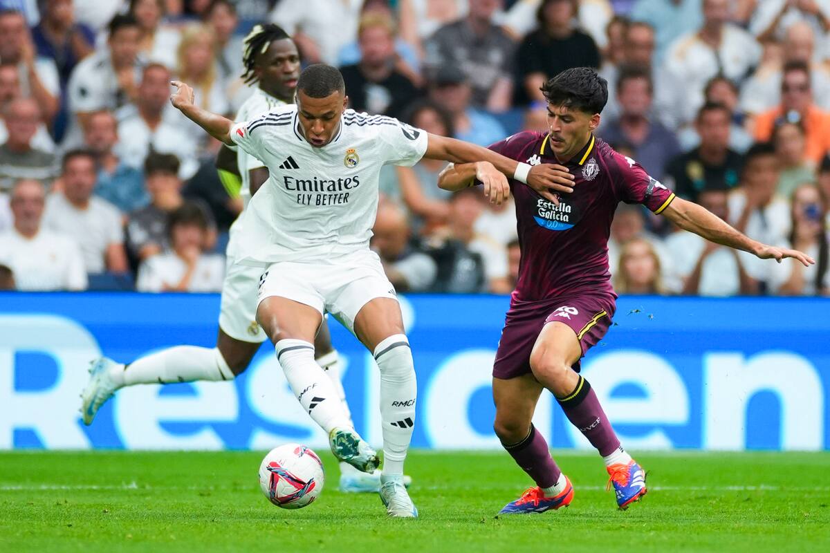 El delantero francés del Real Madrid Kylian Mbappé con el balón perseguido por el centrocampista del Real Valladolid Victor Meseguer (d). //EFE