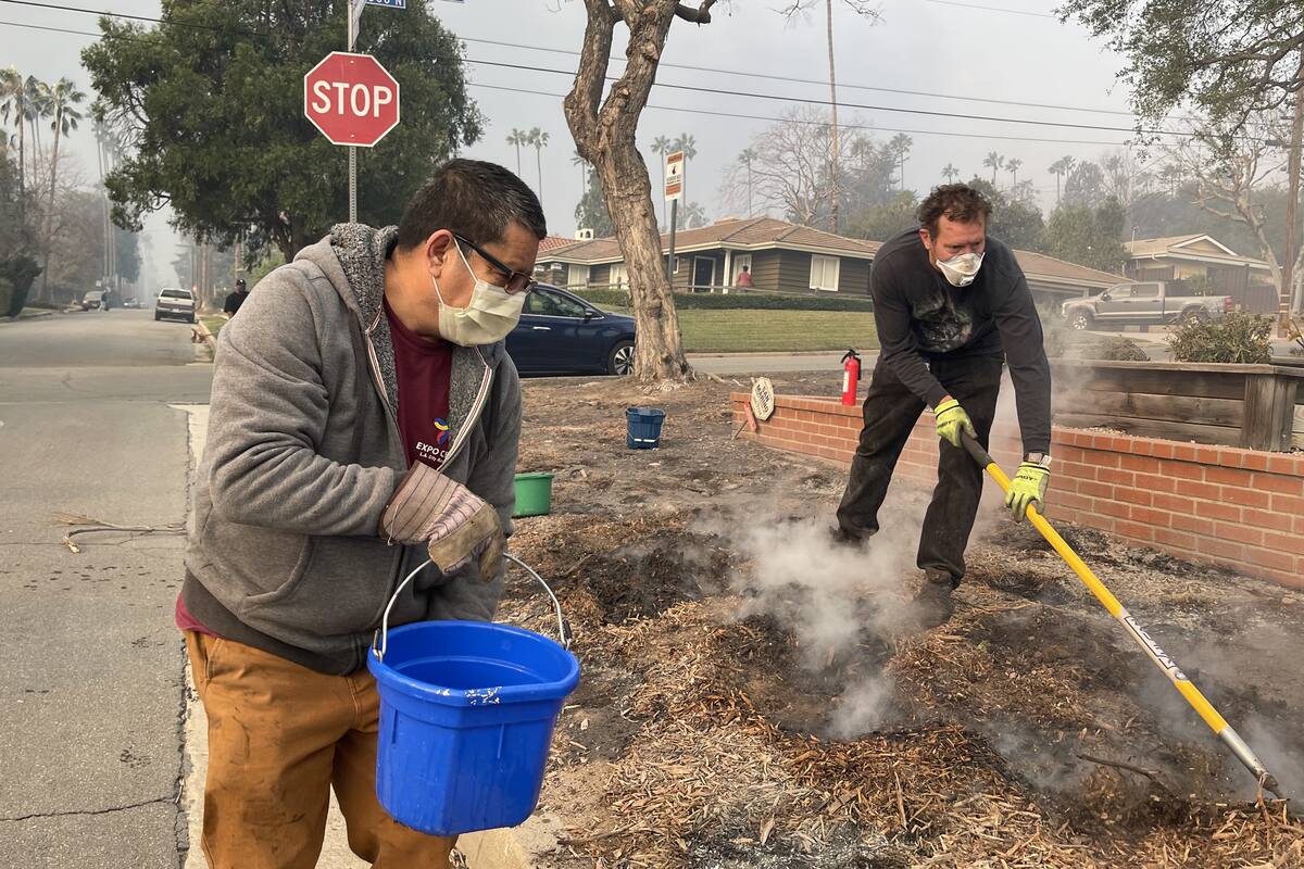 Unas personas vierten agua alrededor de las casas de un vecindario este miércoles, en Altadena, California (Estados Unidos). //EFE