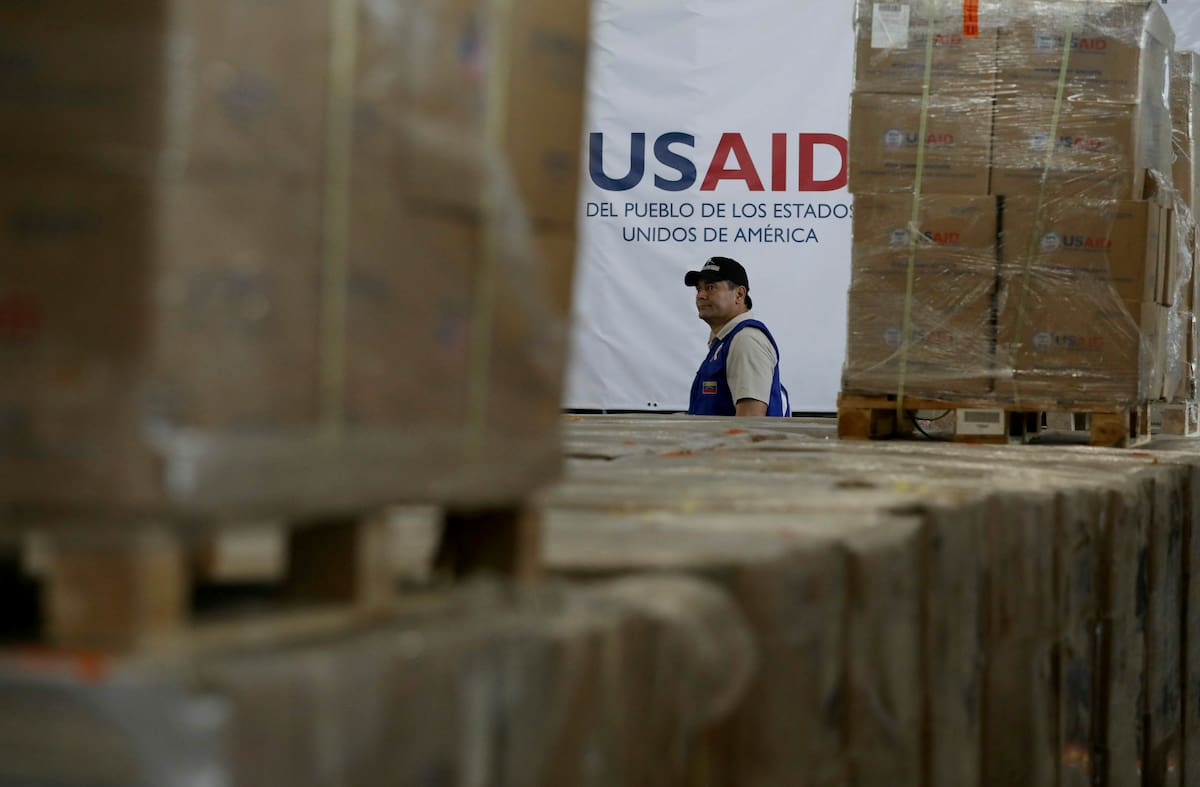Un hombre pasa frente a cajas de ayuda humanitaria de USAID en un almacén en las afueras de Cúcuta. //AP